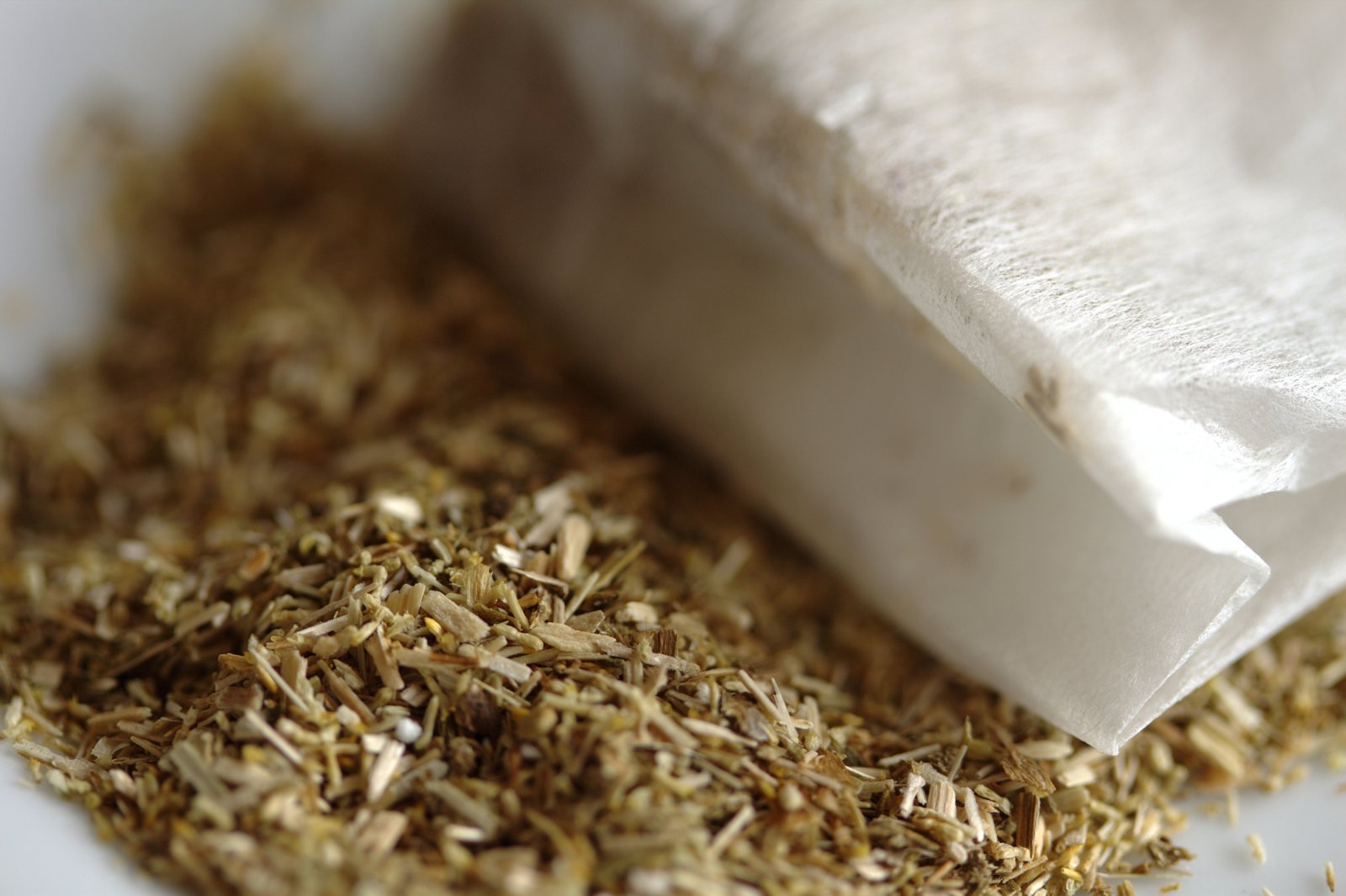 Flores secas de manzanilla saliendo de una bolsita de infusión abierta