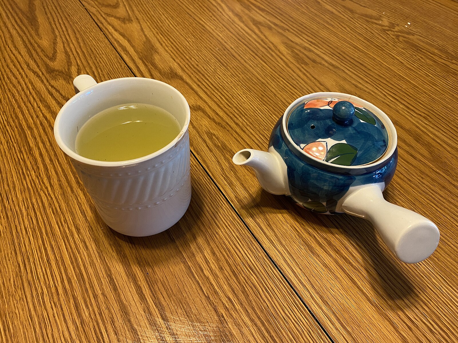Taza de té verde recién preparado junto a una tetera japonesa kyusu sobre una mesa de madera