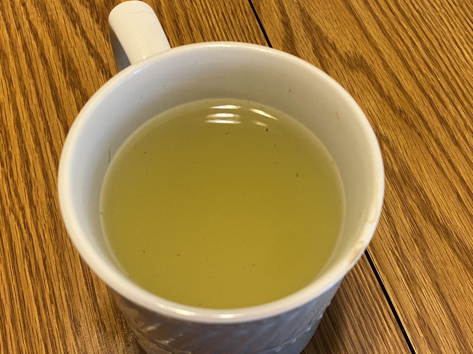 Taza blanca con té verde recién infusionado sobre una mesa de madera